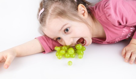 Baby girl lying down and eating green grapes. Studio shot.の写真素材