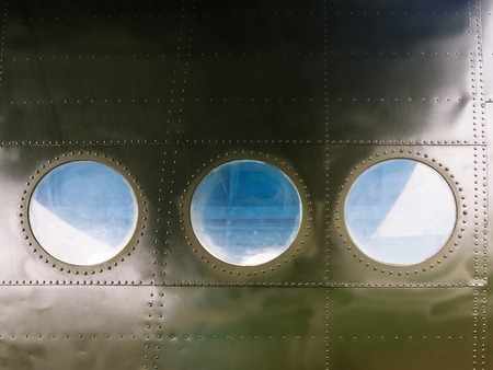 Portholes on military green painted metal background with rivet. Three portholes on board old retro airplane. Outside view of the old aircraft.の写真素材
