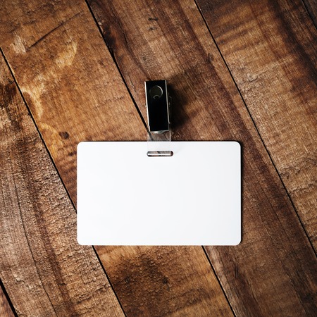 Blank white plastic badge. Template for ID. Blank badge on vintage wooden table background. Mock-up for branding identity for designers. Top view.の写真素材