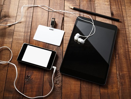 Blank technology template. Tablet with blank screen, smartphone with blank screen, blank badge and headphones on vintage wooden table background. Mock-up for design portfolios.の写真素材
