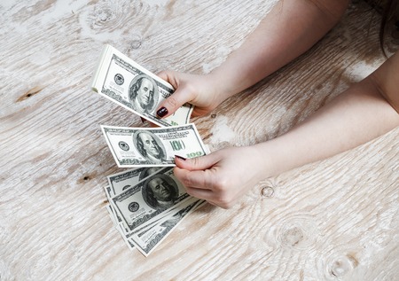 Woman hands with dollars on a wooden background. Cash in hands. Money in hands. Fake money. Shallow depth of field. Selective focus.の写真素材