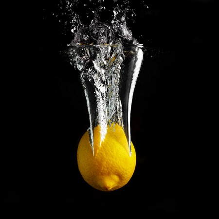 Fresh yellow lemon falling into the water with a splash and air bubbles. Healthy food on black background. Wash fruits.の写真素材