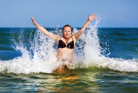 Beautiful girl on a background of blue sea with waves and clear sky on a sunny day. Sexy woman in bikini enjoying a dip in the sea wave.の写真素材