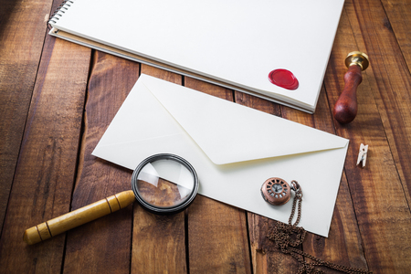 Photo of blank paper envelope, magnifier, seal, stamp and clock on wooden table background. Template for placing your design. Vintage stationery set.の写真素材