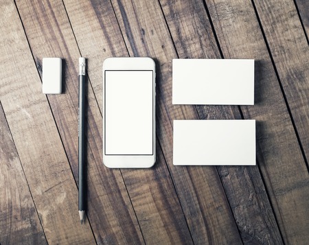 Photo of smartphone with blank screen, business cards, pencil and eraser on wooden table background. Mockup for your design. Business brand template. Top view.の写真素材