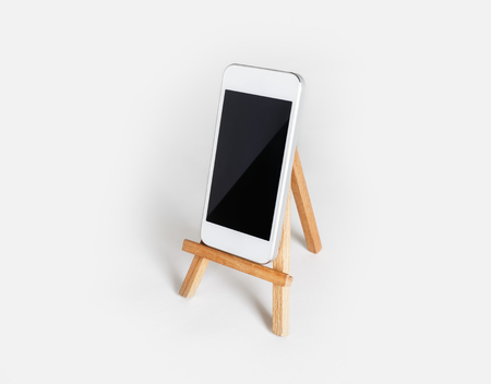 Smartphone with blank screen on wooden stand at white paper background. Mockup for placing your designの写真素材
