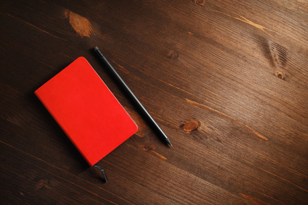 Blank red notebook and pencil on wood table background. Template for branding identity. Flat lay.の写真素材