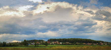 Picturesque rural landscape. Scenic sky with clouds, houses and trees. Panoramic shot.の写真素材