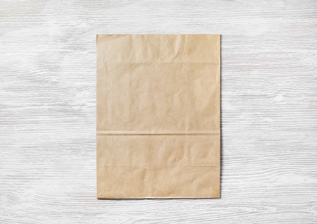 Crumpled kraft paper bag on light wooden background. Blank recyclable package. Top view. Flat lay.の写真素材