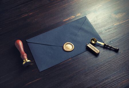Photo of vintage black envelope with wax seal, stamp and spoon on dark wood table background.の写真素材