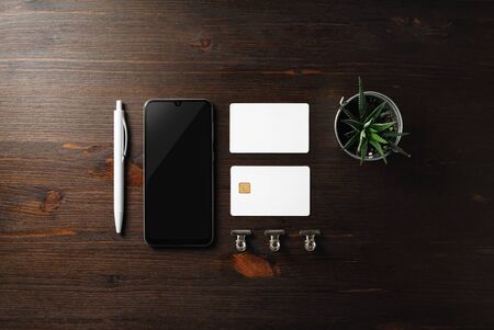 Blank business template. Smartphone, business card, bank card, pen and plant on wood table background. Flat lay.の写真素材