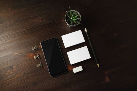 Blank stationery and smartphone on wood table background. Smartphone, business cards, pencil, eraser...