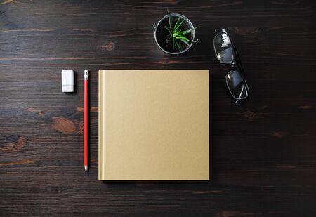 Blank book and stationery on wooden background. Notepad, glasses, pencil, eraser and plant. Flat...