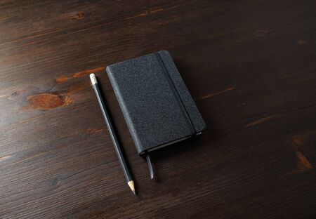 Photo of black notepad and pencil on wood table background.の写真素材