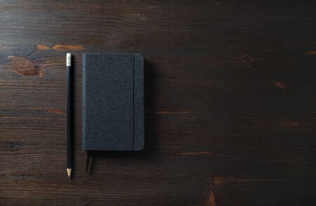 Black notepad and pencil on wood table background. Responsive design template.
