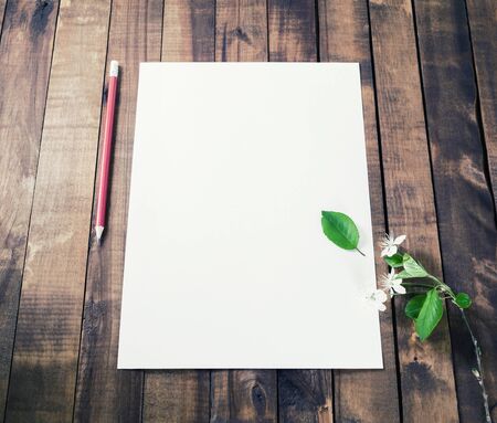 Blank white letterhead, pencil, eraser and cherry flowers on vintage wooden table background....