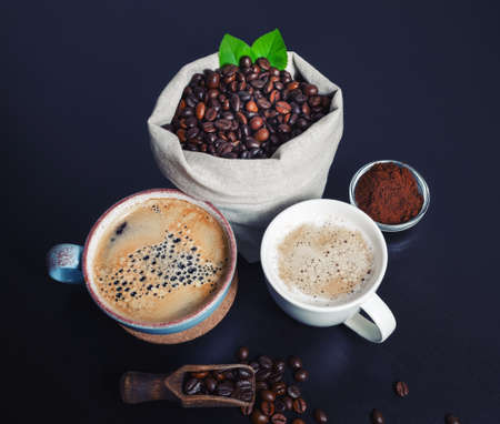 Hot coffee cups and coffee beans in canvas bag and ground powder on black kitchen table background.の写真素材