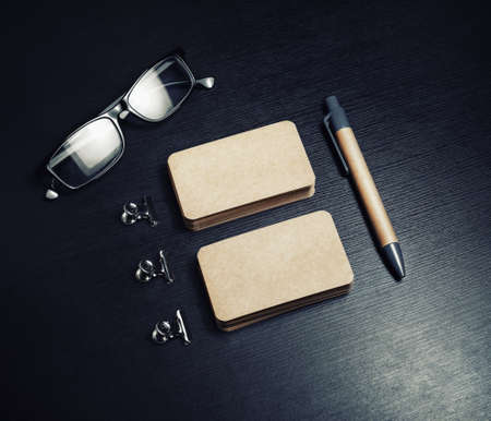 Blank kraft business cards, pen and glasses on black wooden background. Template for branding...