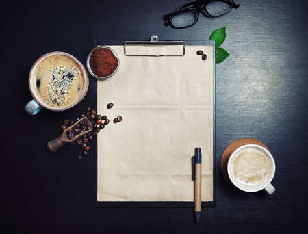 Clipboard with blank kraft letterhead, coffee cups, roasted coffee beans, pen and coffee ground on black table background. Space for text. Top view. Flat lay.の写真素材