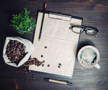 Menu and coffee. Clipboard with blank kraft letterhead, coffee cup, coffee beans, glasses, pencil and plant on wooden background. Top view. Flat lay.の写真素材