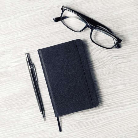 Black notebook, glasses and mechanical pencil on light wooden background. Top view. Flat lay.の写真素材