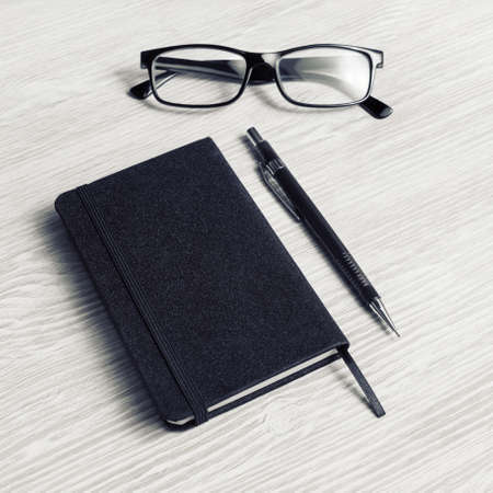 Blank black notepad, glasses and pencil on light wooden background.の写真素材