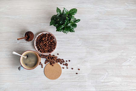 Delicious fresh coffee. Coffee cup, roasted coffee beans, plant, beer coaster and ground powder on light wooden background. Flat lay.の写真素材