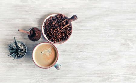 Tasty coffee background. Coffee cup, coffee beans, plant and ground powder on light wood kitchen table. Top view. Flat lay.の写真素材