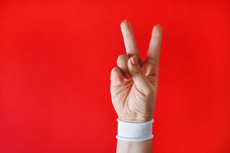 Female hand with white bracelet shows victory sign on red backgroung.の写真素材