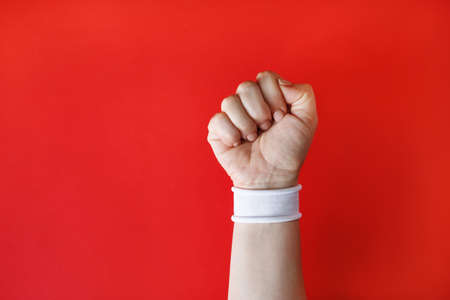 Clenched fist female hand with white bracelet on red backgroung.