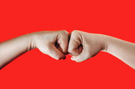 Two female fists hitting each other on red background. Hands clenched into fists. Fight concept.の写真素材