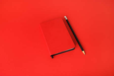 Red notebook and pencil on red paper background. Template for branding identity.の写真素材
