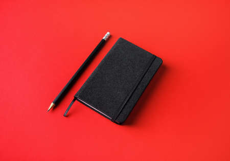Blank black notebook and pencil on red paper background.の写真素材