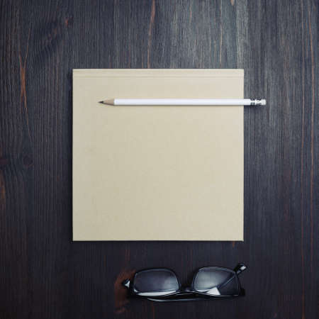 Photo of blank closed brochure, pencil and glasses on wooden background. Responsive design mockup....