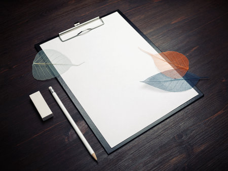 Clipboard with blank white sheet of paper, pencil, leaves and eraser on wooden background. Responsive design template.の写真素材
