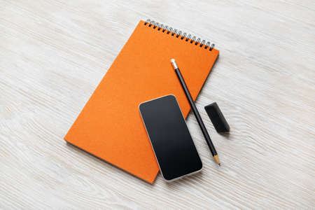 Blank orange notepad, smartphone, pencil and eraser on light wood table background.の写真素材