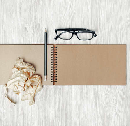 Blank open sketchbook, glasses, pencil and crumpled paper on light wooden background. Responsive design mockup. Top view. Flat lay.の写真素材