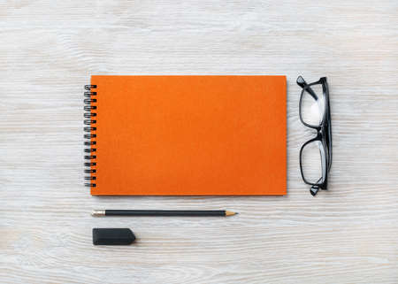 Orange notebook, glasses, pencil and eraser on light wood table background. Top view. Flat lay.