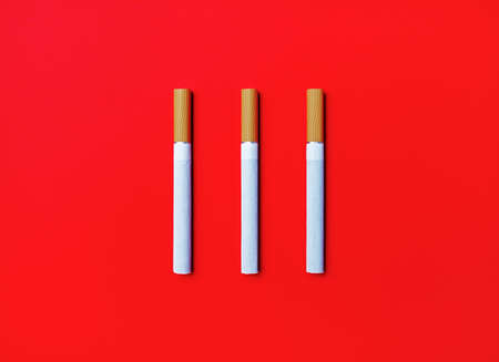 Three cigarettes on red background. Flat lay.の写真素材