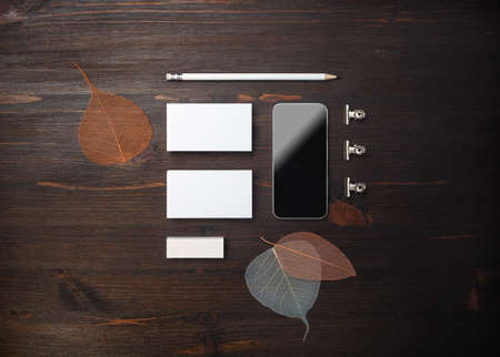 Branding stationery set. Blank business cards, smartphone, pencil, eraser and leaves on wooden background. ID mockup. Responsive design template. Flat lay.の写真素材