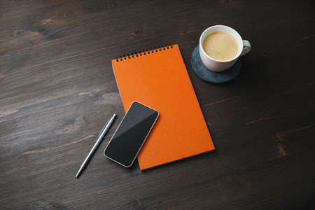 Smartphone, blank notepad, coffee cup and pen on wooden background. Template for placing your design.の写真素材
