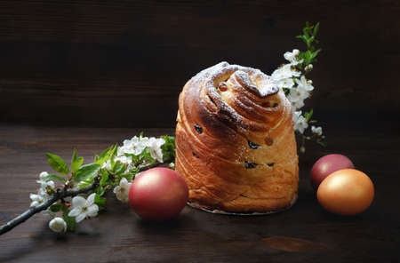 Sweet bun, easter eggs and spring flowers on wooden background.