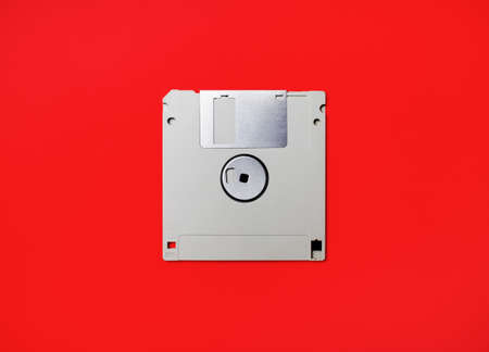Gray diskette on red paper background. Floppy disc. Flat lay.の写真素材