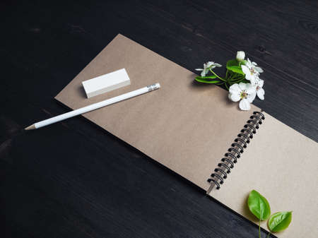 Photo of blank kraft notebook, pencil, eraser and spring flowers on wood table background.