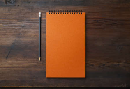 Blank orange notebook and pencil on wooden background. Stationery mock up. Flat lay.の写真素材
