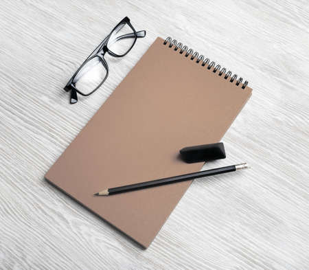 Mockup of vintage stationery. Blank kraft notepad, pencil eraser and glasses on light wooden...