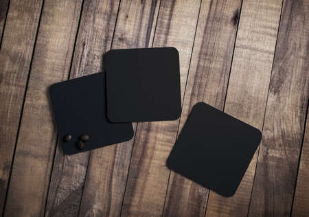 Photo of three blank black square beer coasters and coffee beans on wood table background. Top view. Flat lay.の写真素材