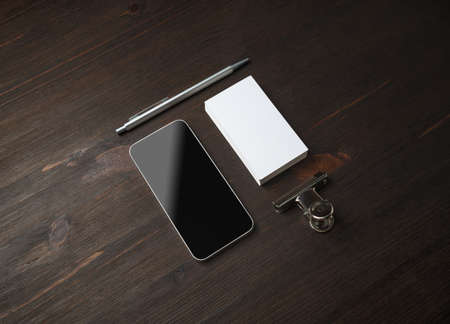 Smartphone and blank stationery: business card, pen and paper clip on wood table background....