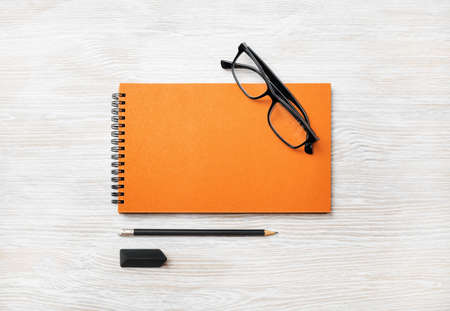 Blank orange notebook, glasses, pencil and eraser on light wood table background. Template for branding design. Flat lay.の写真素材