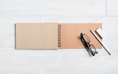 Blank open craft notebook, glasses, pencil and eraser on wooden background. Flat lay.